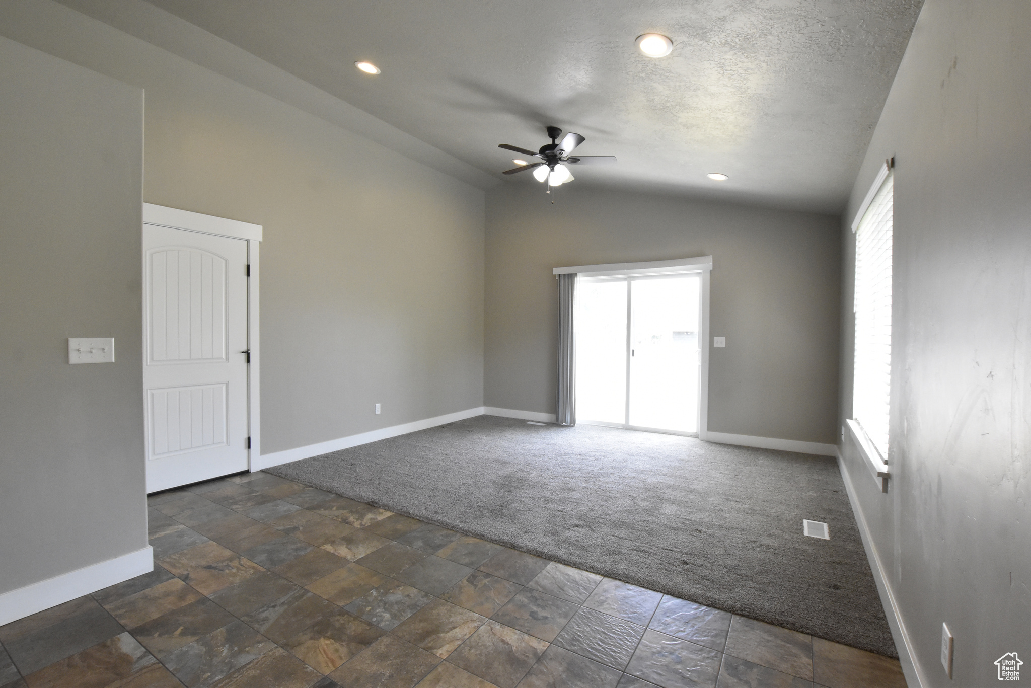 Carpeted spare room featuring a textured ceiling, vaulted ceiling, and ceiling fan