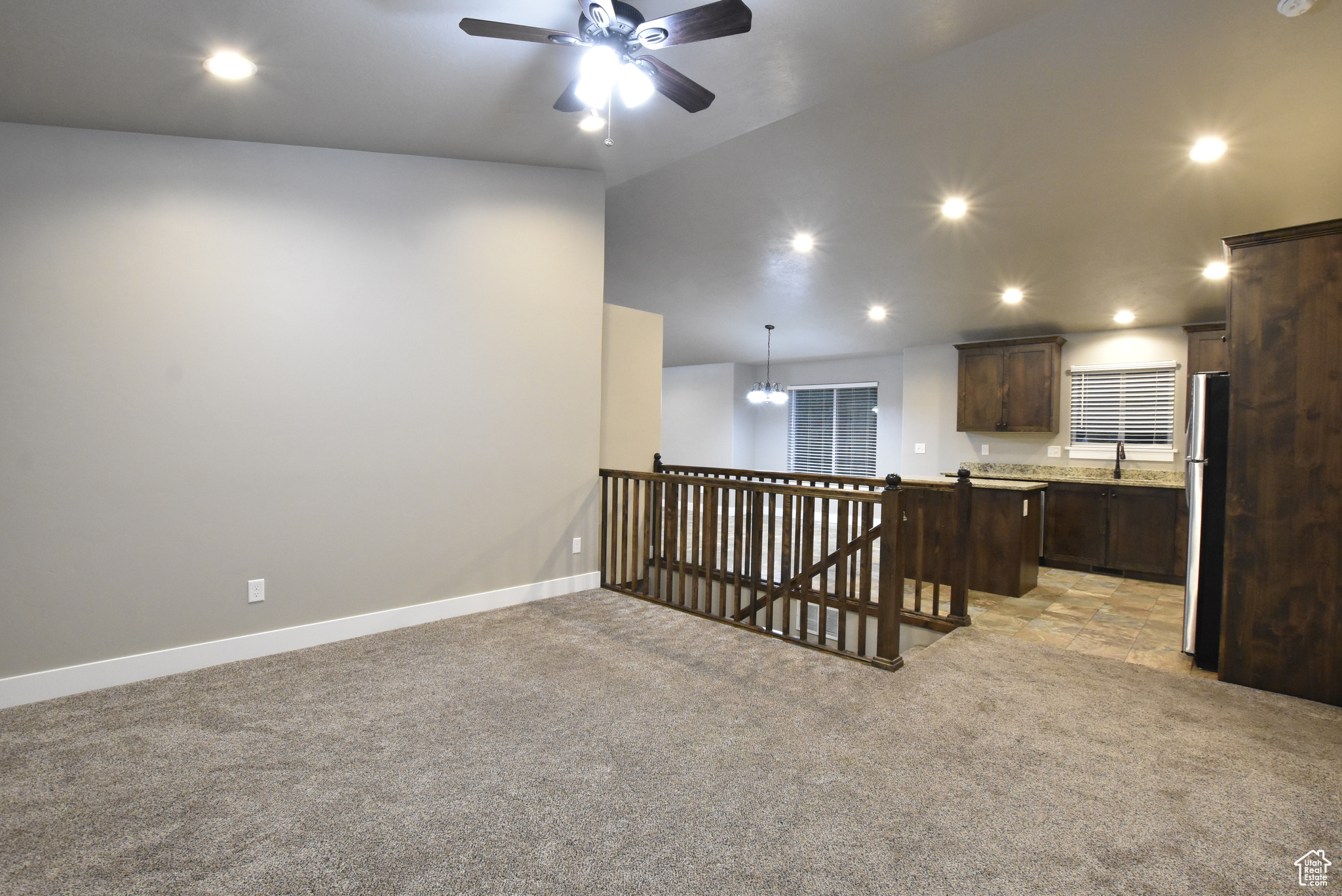 Empty room featuring ceiling fan with notable chandelier, light colored carpet, and sink