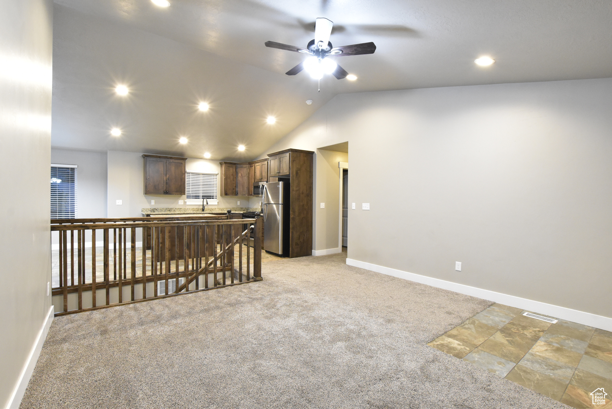 Kitchen with carpet flooring, dark brown cabinetry, ceiling fan, stainless steel refrigerator, and lofted ceiling