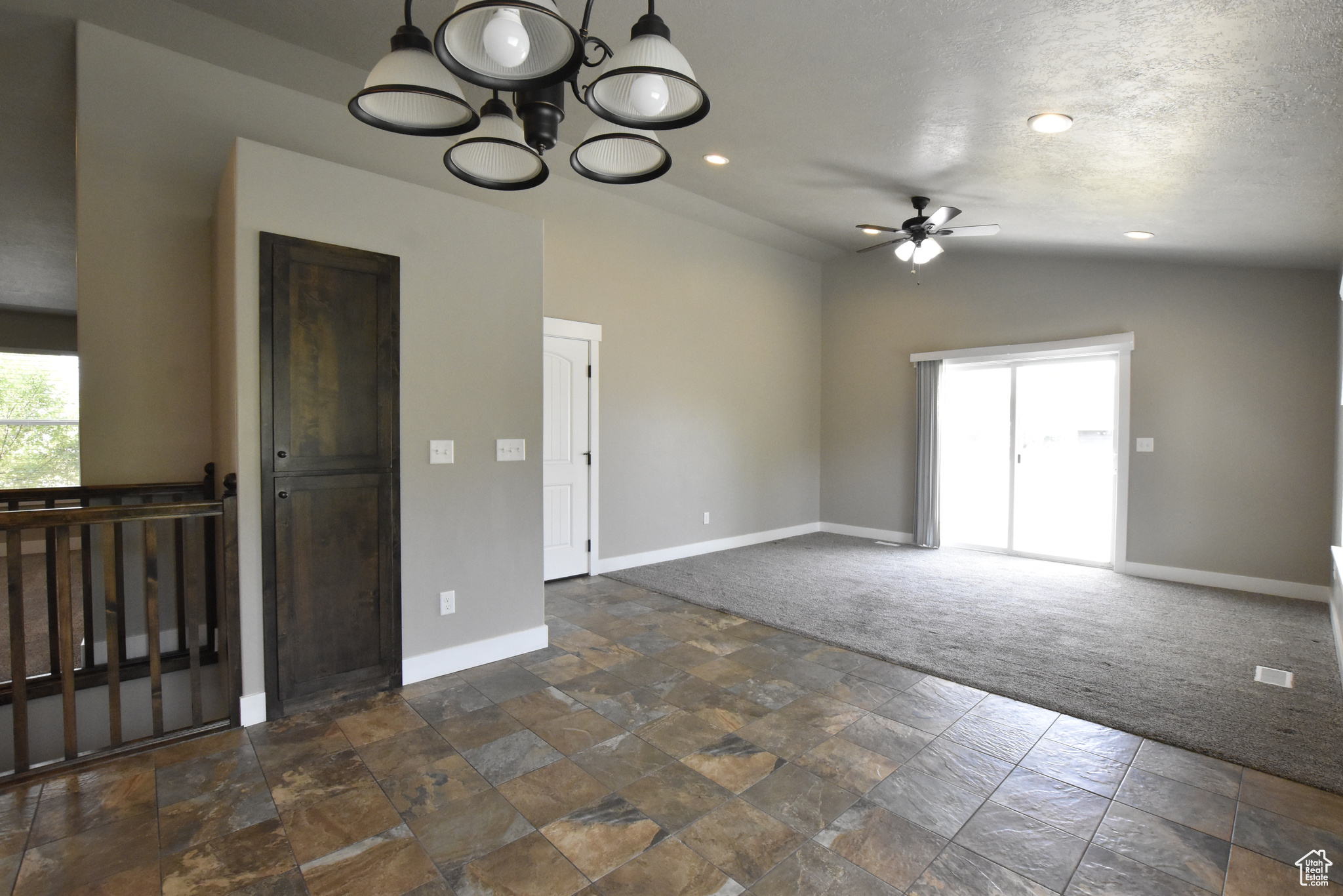 Unfurnished room with a textured ceiling, ceiling fan with notable chandelier, dark carpet, and lofted ceiling