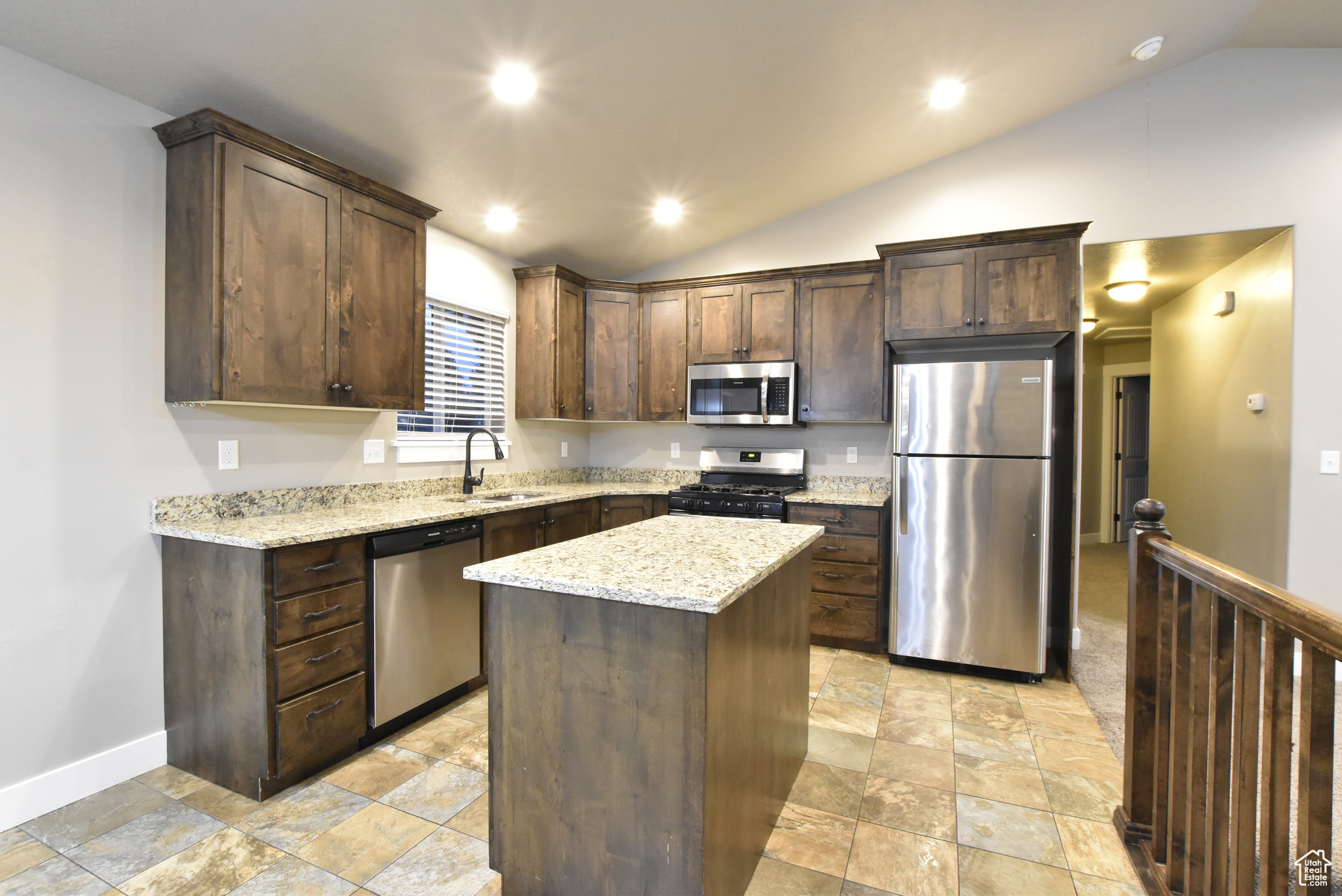 Kitchen with appliances with stainless steel finishes, vaulted ceiling, a kitchen island, and sink