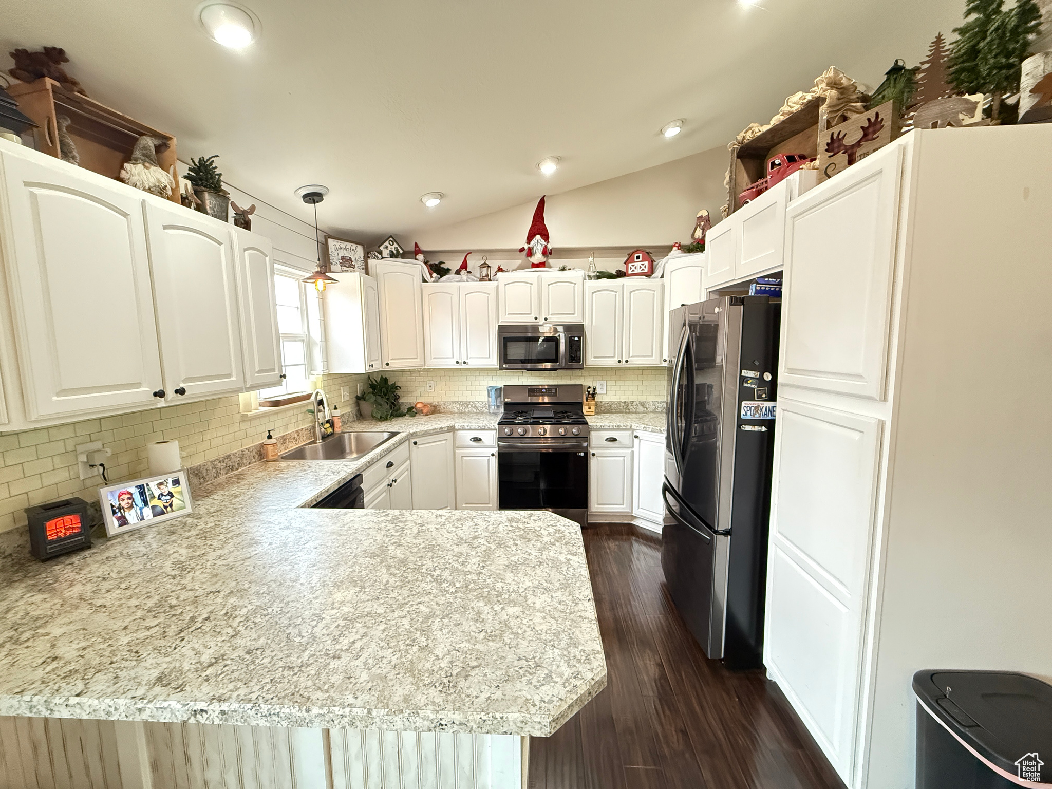 Kitchen with stainless steel appliances, sink, decorative light fixtures, white cabinetry, and lofted ceiling