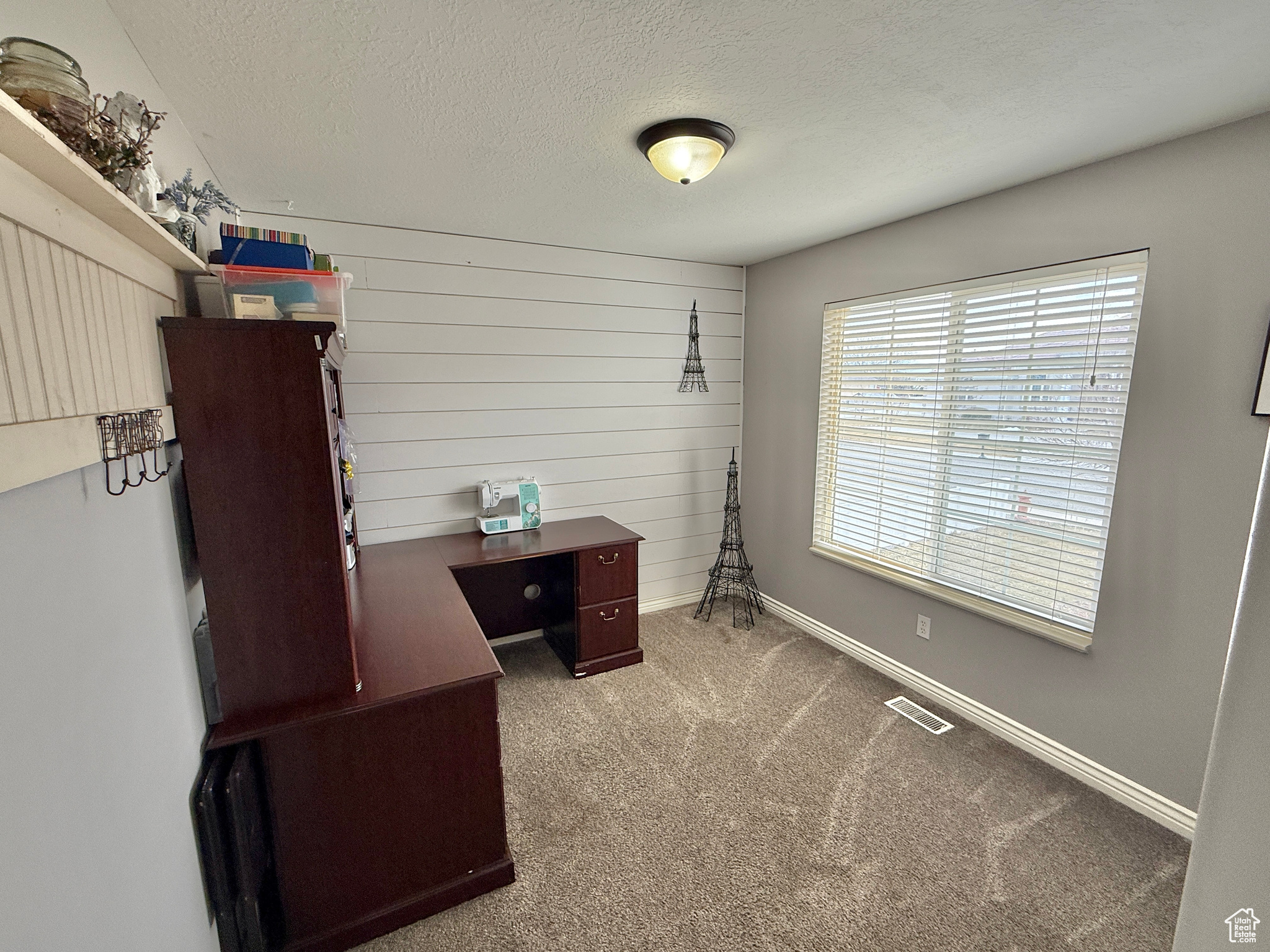 Office area featuring wooden walls, light colored carpet, and a textured ceiling