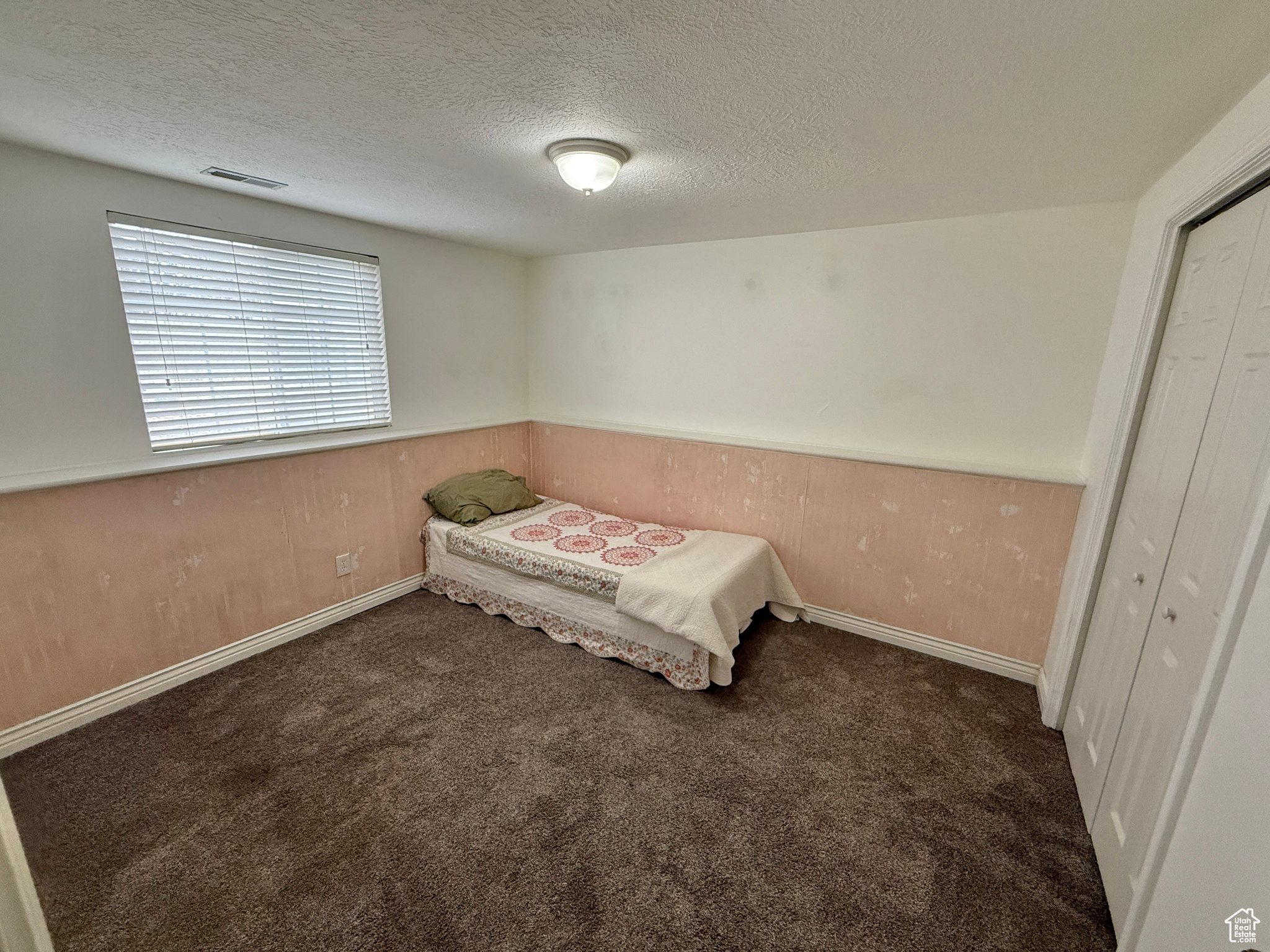 Unfurnished bedroom featuring dark colored carpet, a textured ceiling, wooden walls, and a closet
