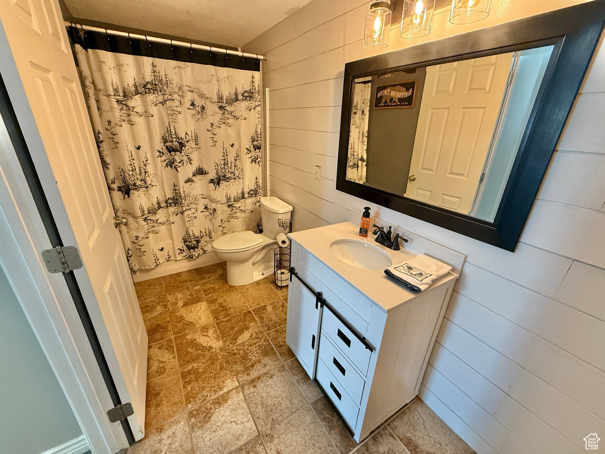 Bathroom with a shower with curtain, vanity, wood walls, and toilet
