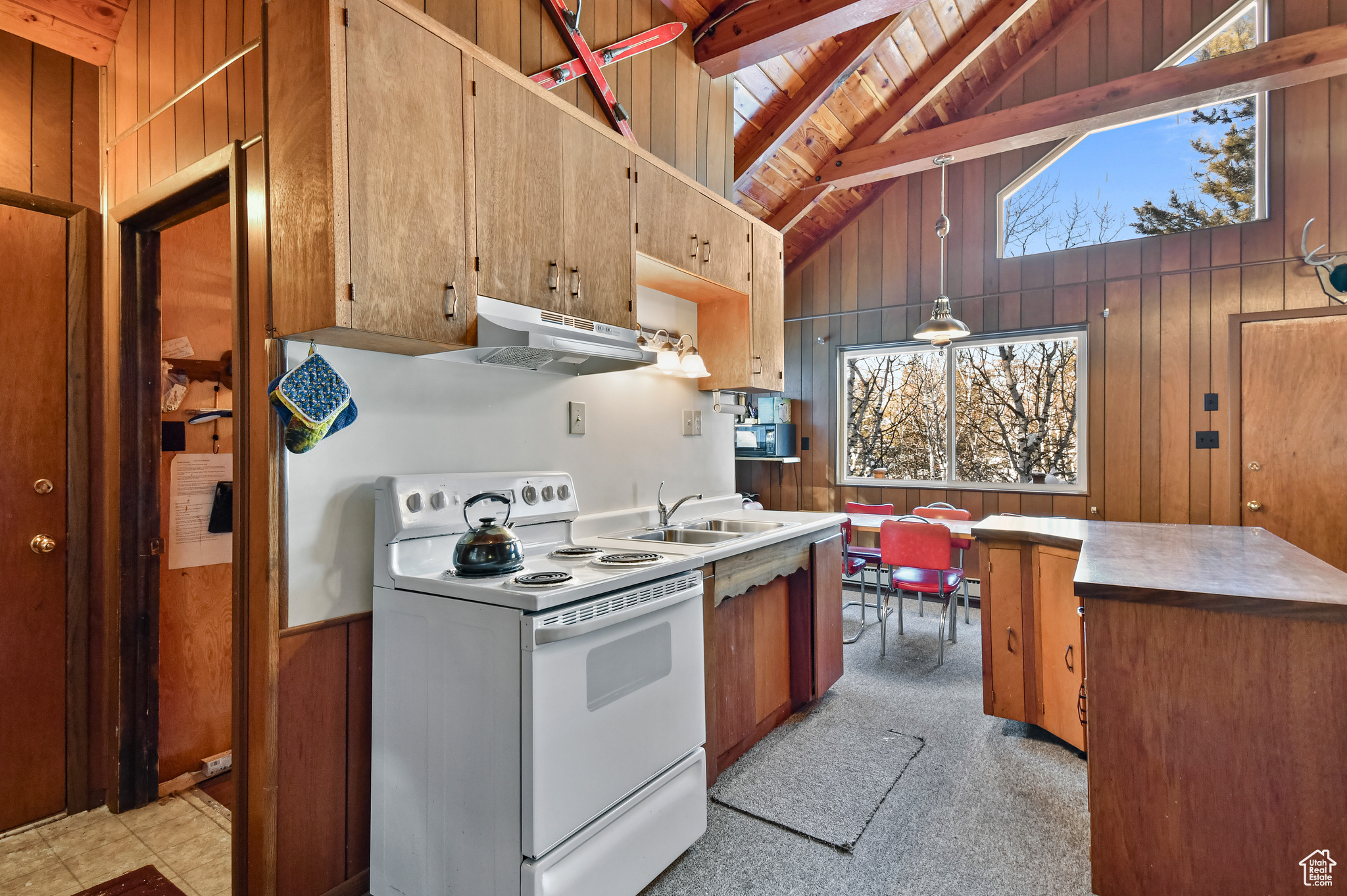Kitchen with sink, exhaust hood, beam ceiling, electric range, and wood walls