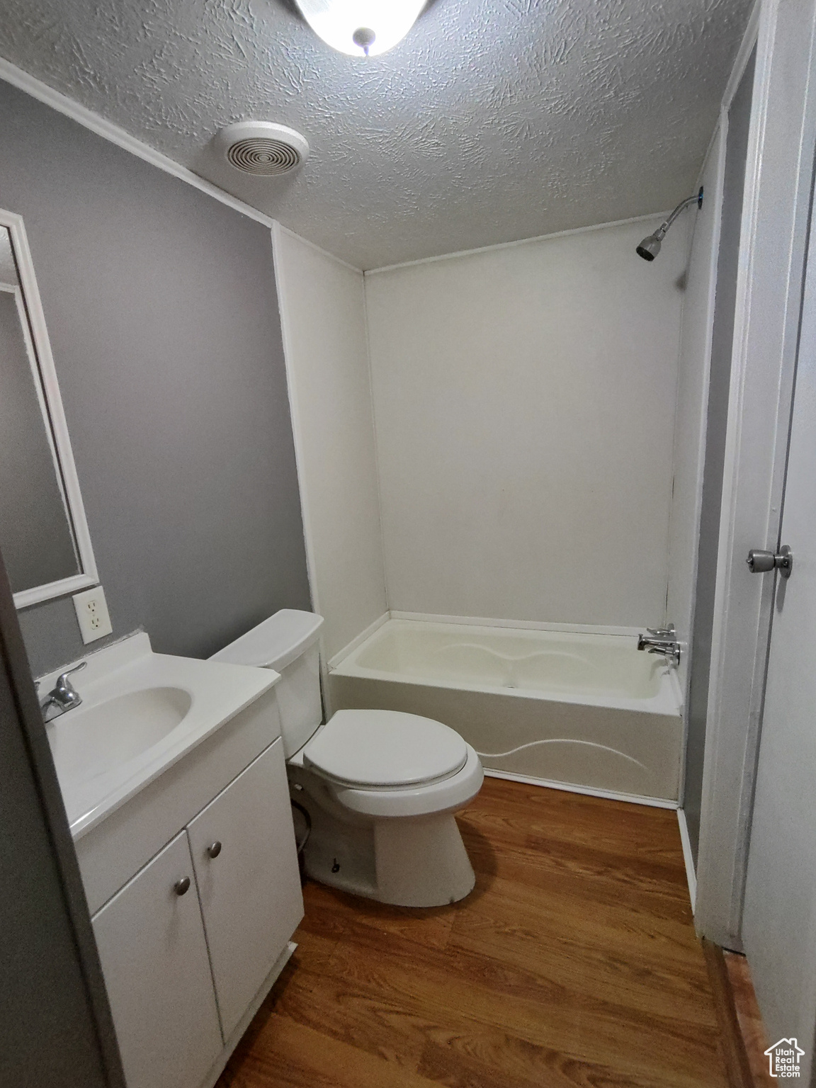 Full bathroom featuring washtub / shower combination, hardwood / wood-style floors, a textured ceiling, toilet, and vanity