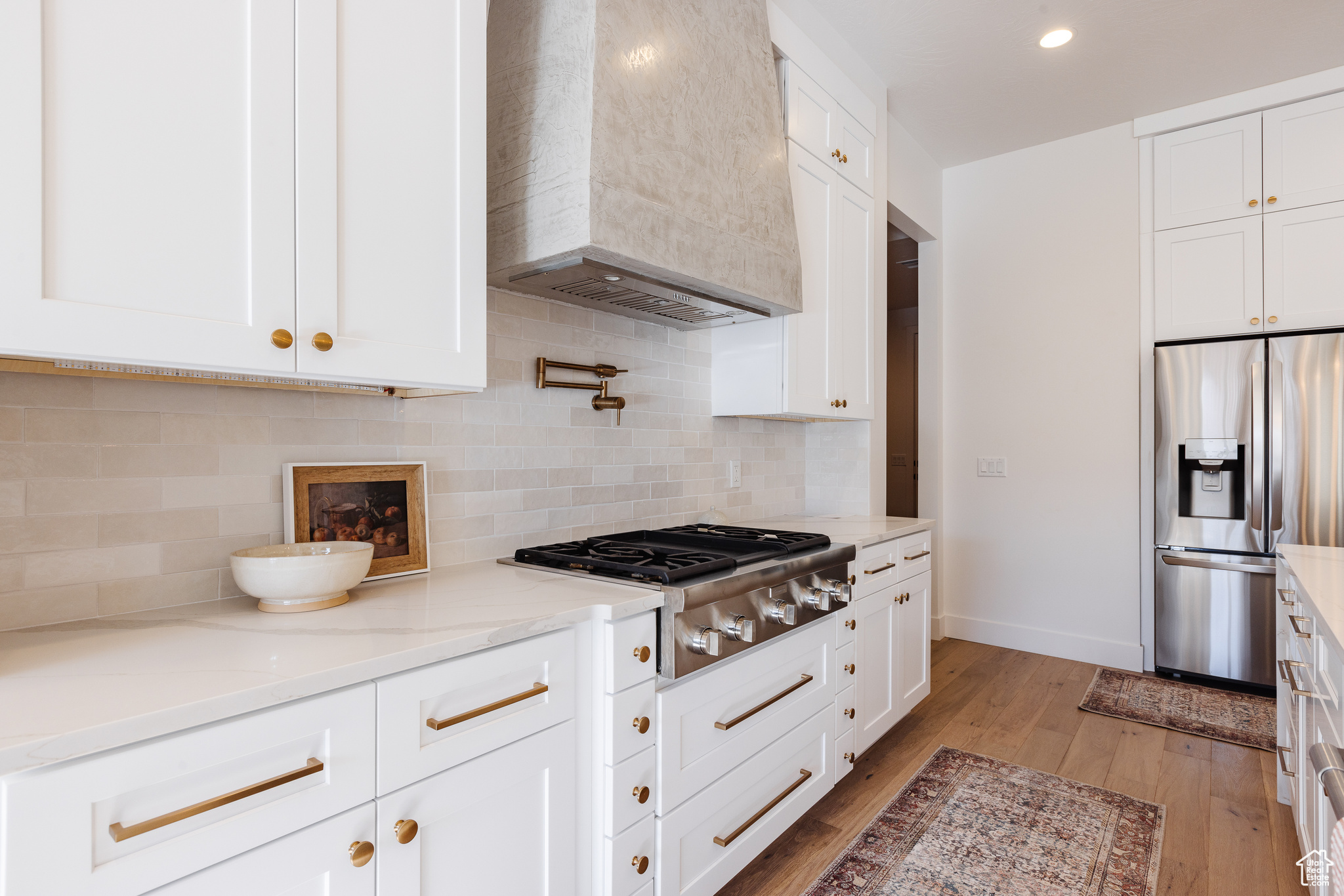 Kitchen with white cabinetry, stainless steel appliances, wall chimney range hood, light stone counters, and light wood-type flooring