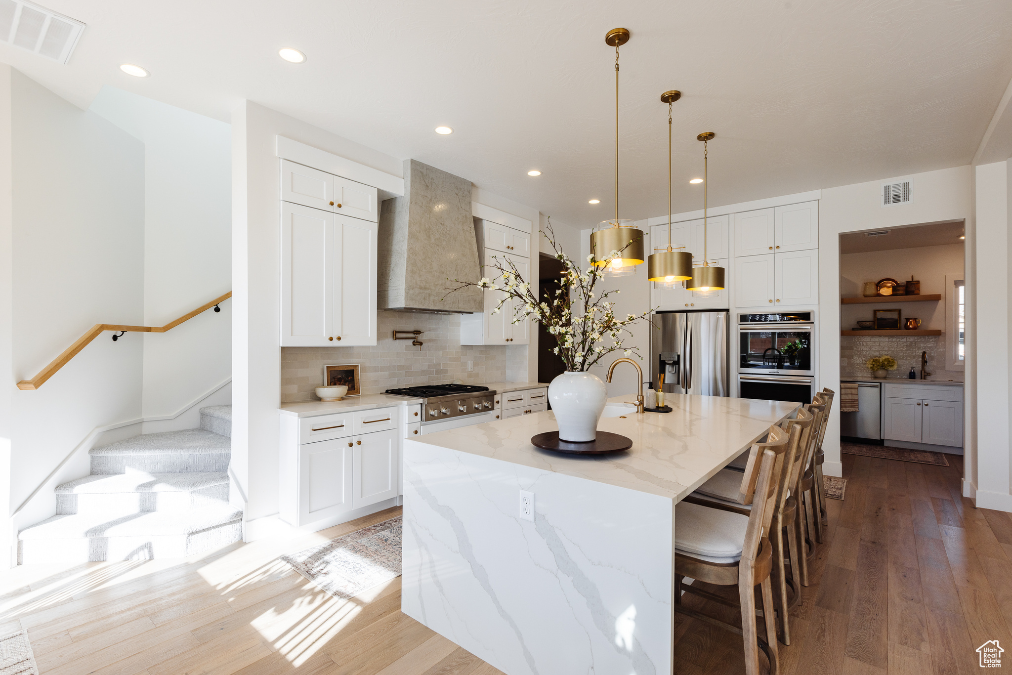 Kitchen with light stone countertops, wall chimney exhaust hood, backsplash, a spacious island, and appliances with stainless steel finishes