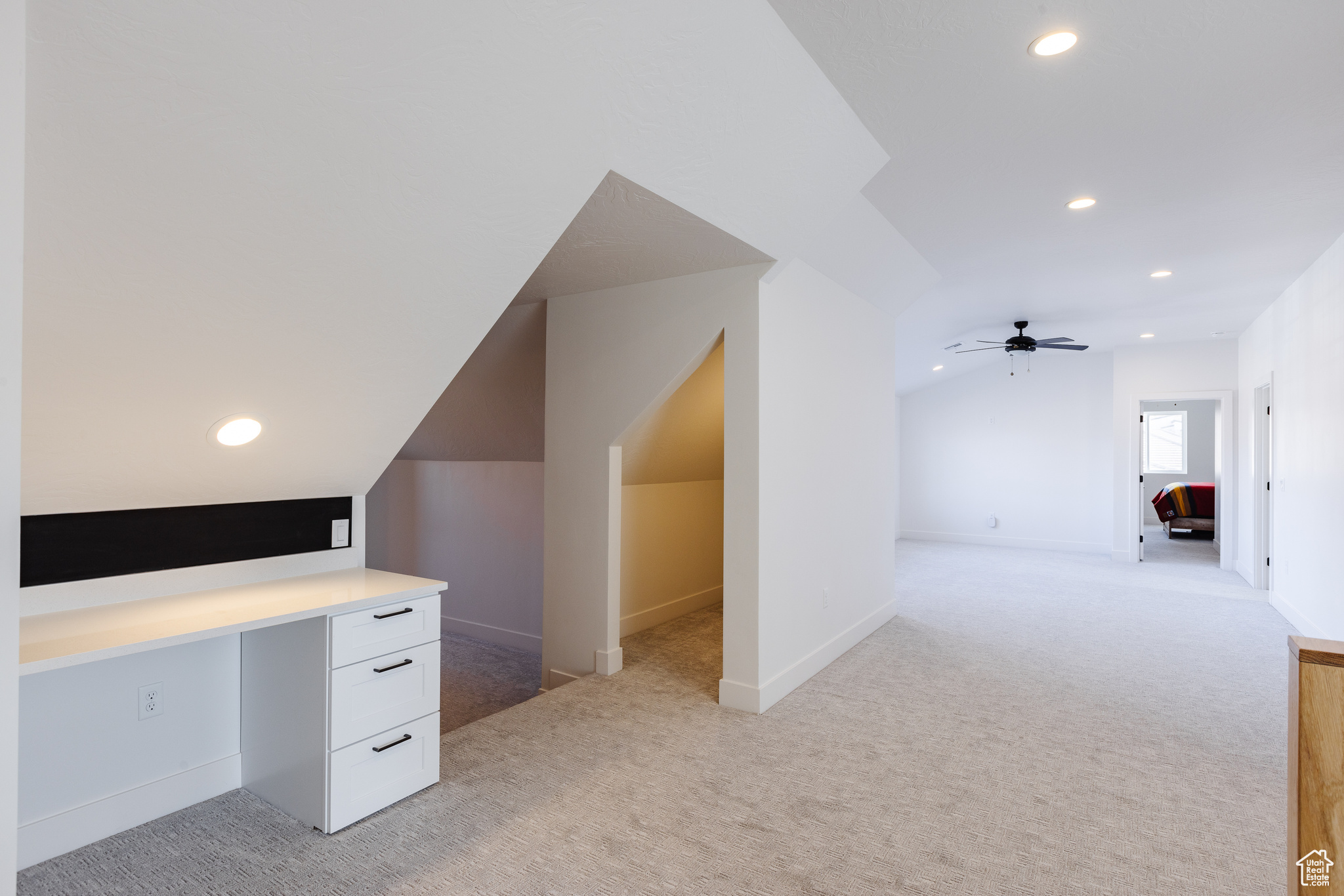 Bonus room featuring ceiling fan, light colored carpet, built in desk, and lofted ceiling