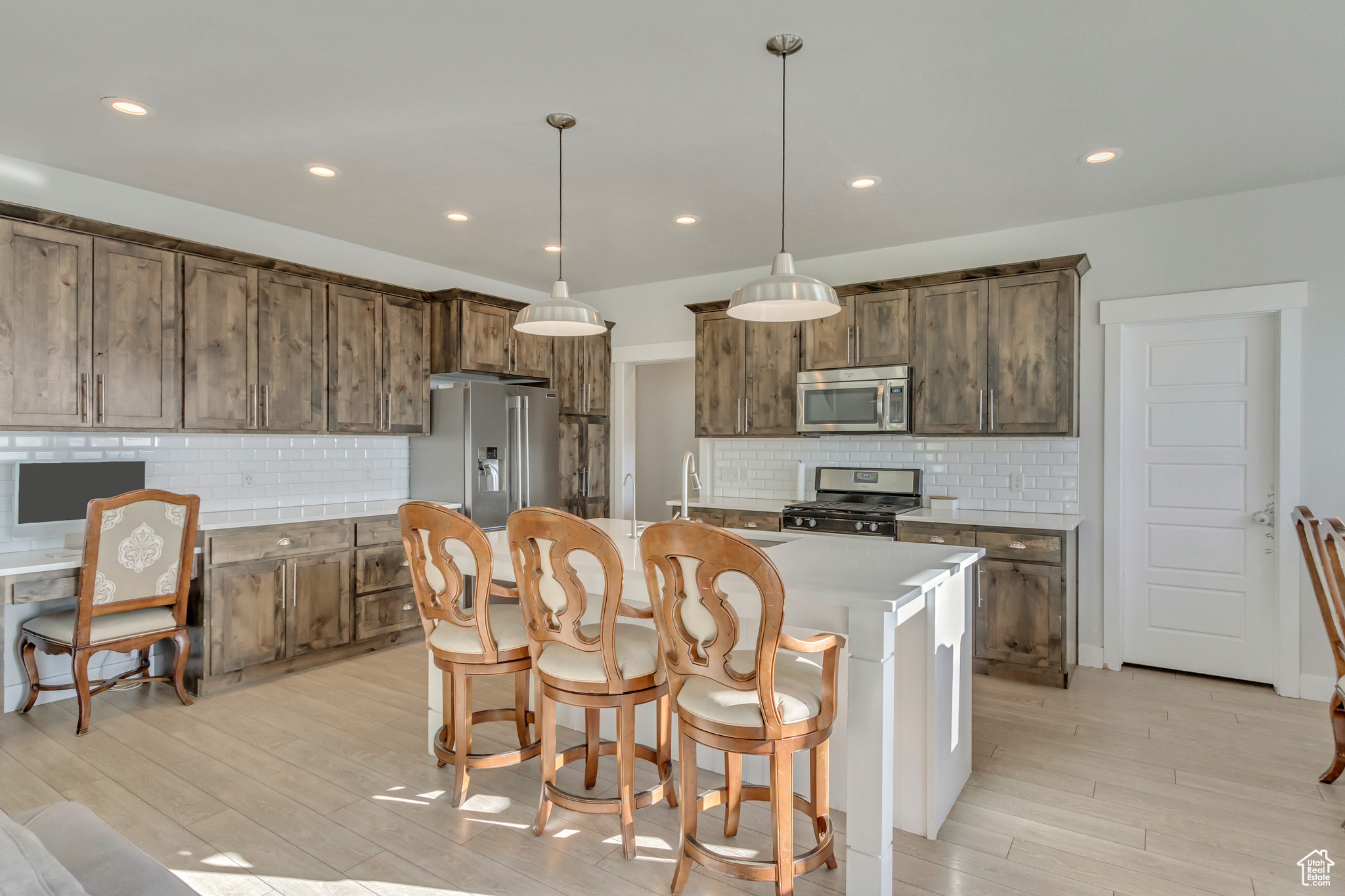 Kitchen featuring stainless steel appliances, backsplash, an island with sink, and hanging light fixtures