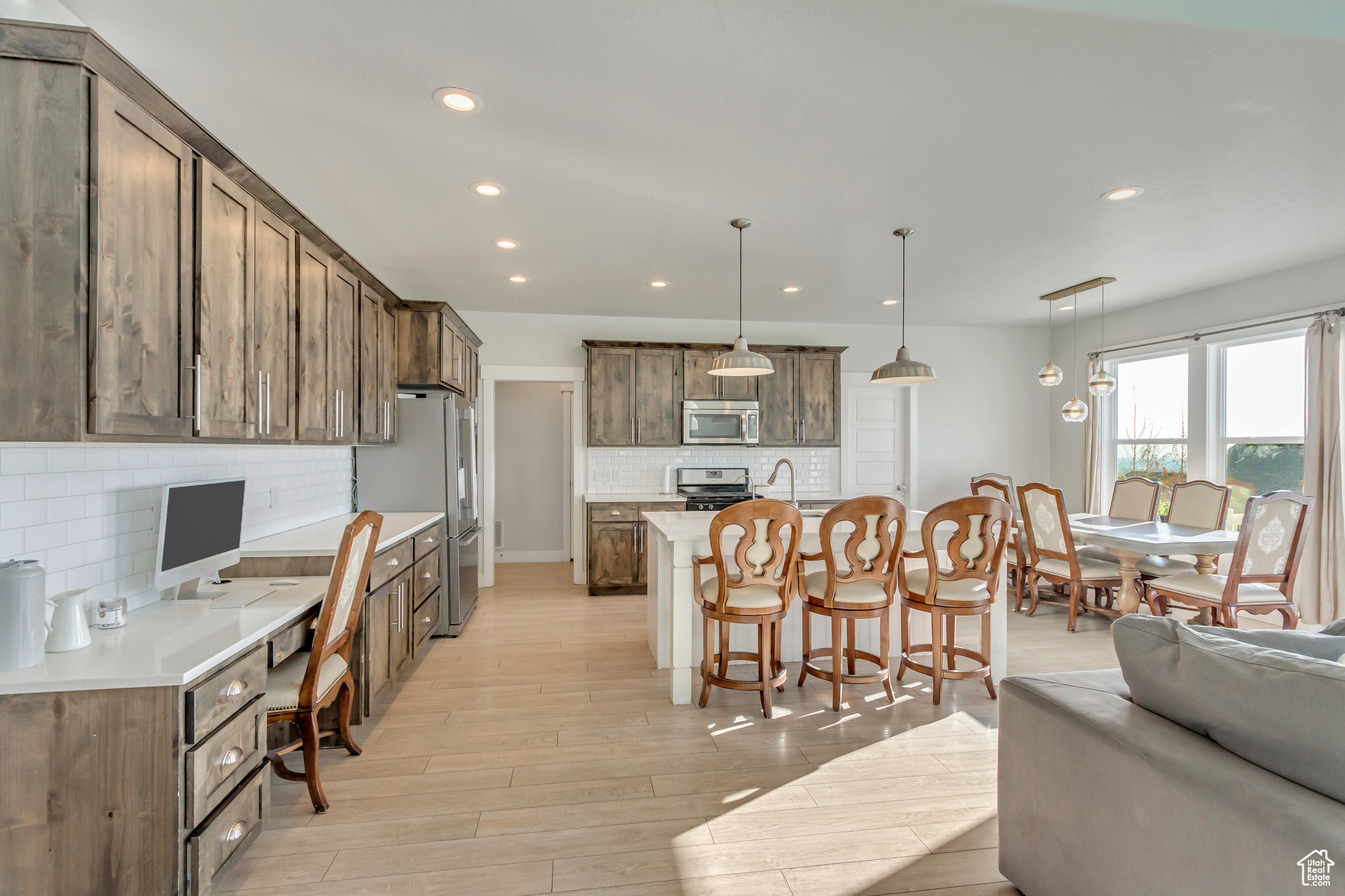 Kitchen with decorative light fixtures, decorative backsplash, an island with sink, and appliances with stainless steel finishes