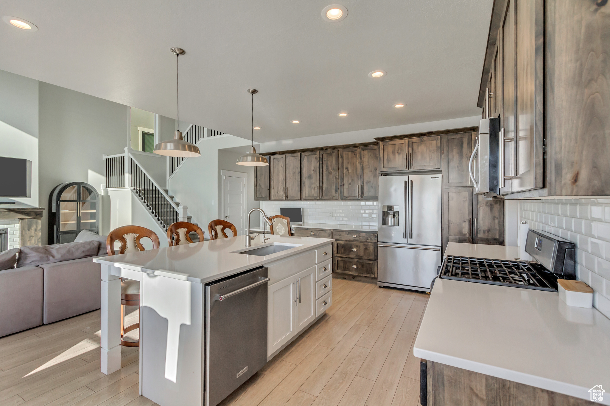 Kitchen featuring decorative light fixtures, an island with sink, white cabinets, appliances with stainless steel finishes, and sink