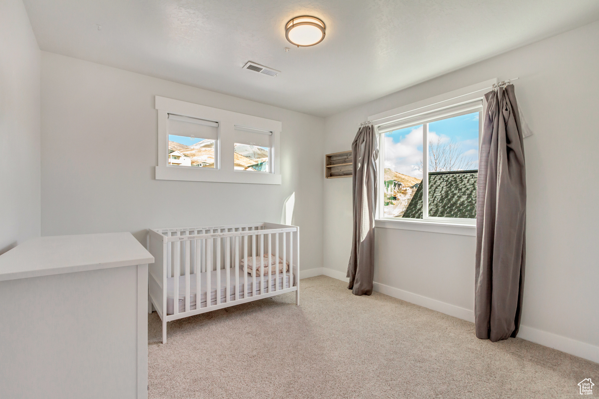 Bedroom featuring light colored carpet and a nursery area