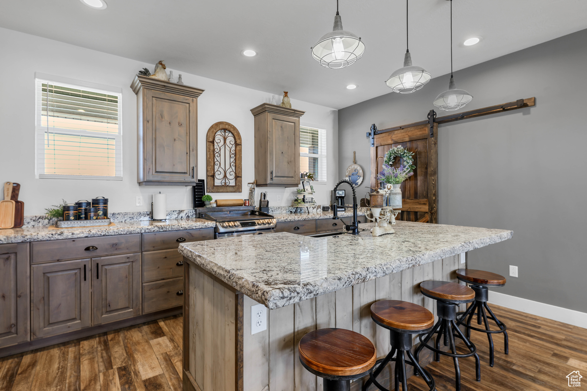 Kitchen featuring pendant lighting, a barn door, light stone countertops, and an island with sink