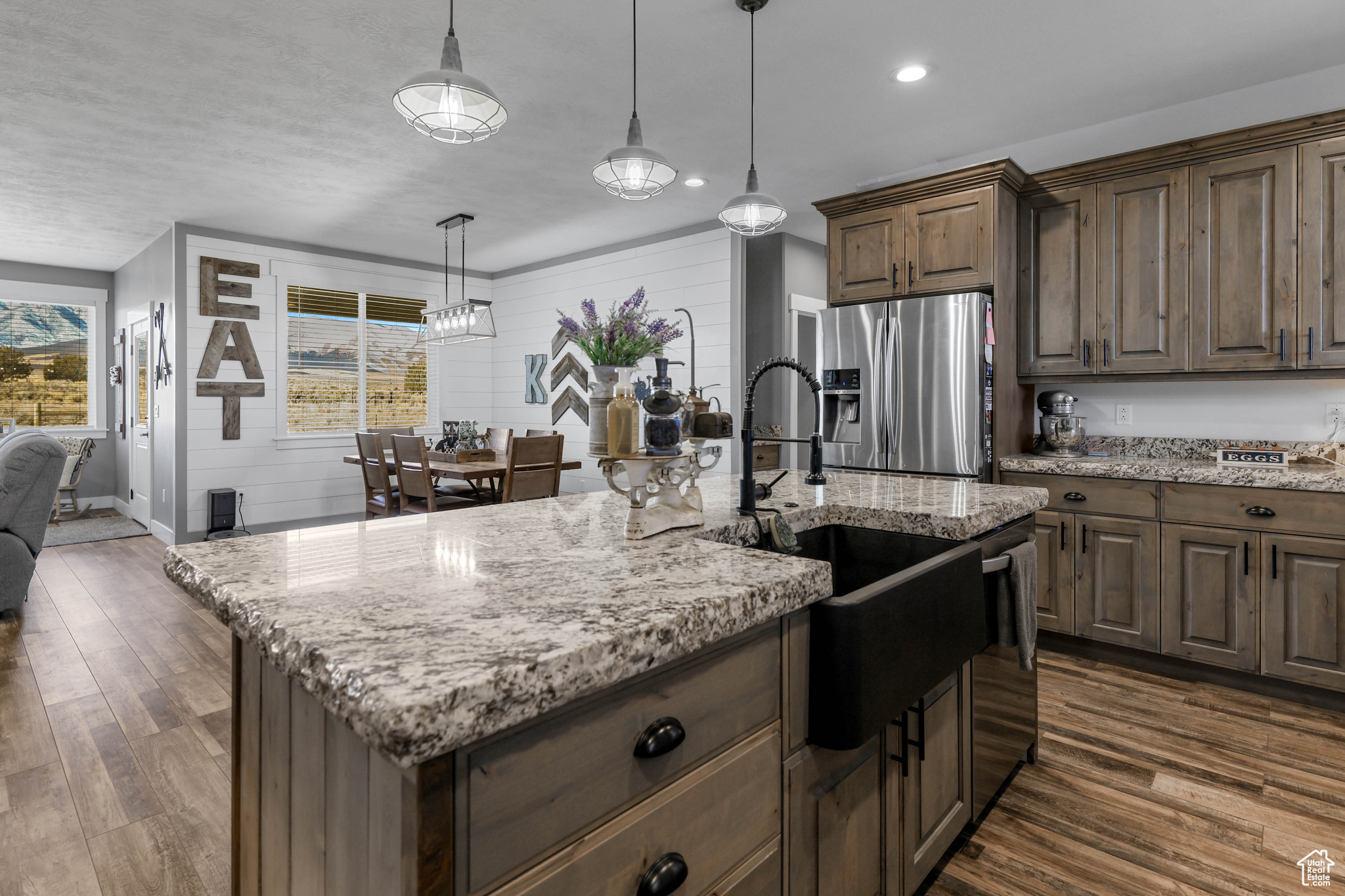 Kitchen with sink, an island with sink, decorative light fixtures, dark hardwood / wood-style flooring, and stainless steel fridge with ice dispenser