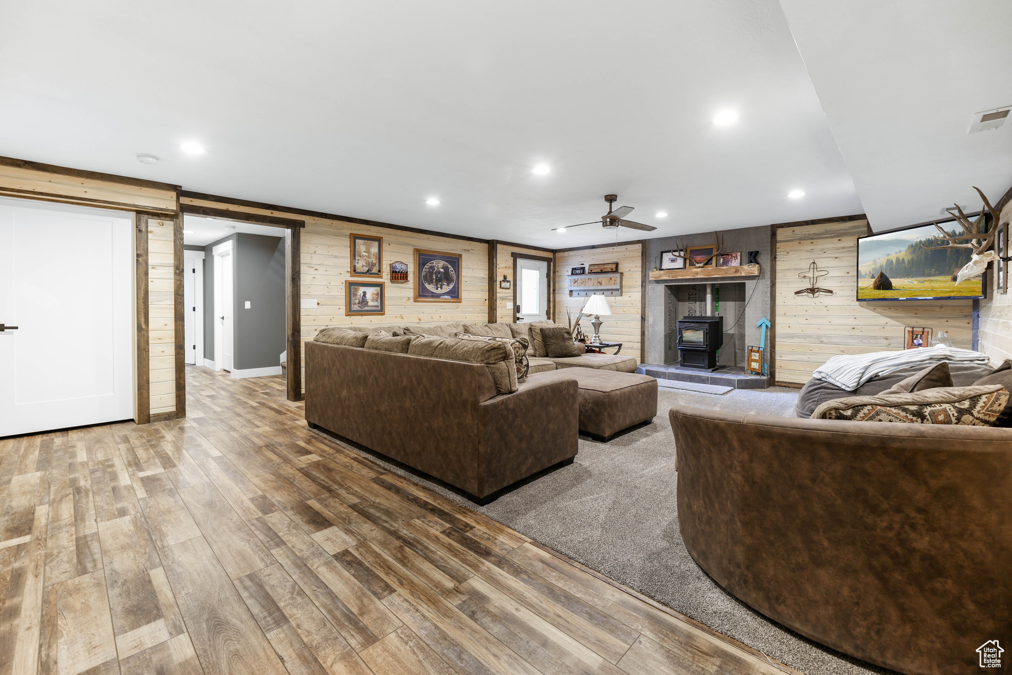 Living room featuring wood-type flooring, a wood stove, ceiling fan, and wooden walls