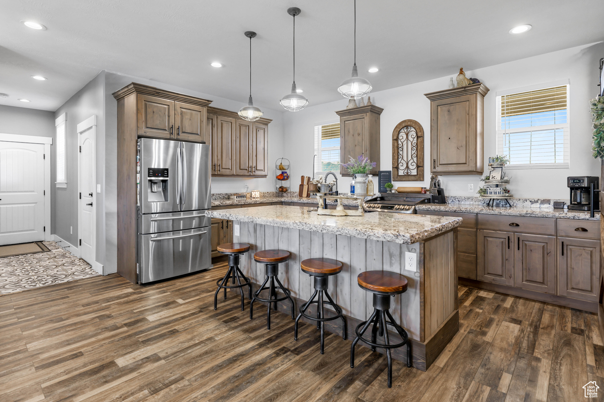 Kitchen with light stone countertops, stainless steel refrigerator with ice dispenser, dark hardwood / wood-style floors, and a kitchen island with sink