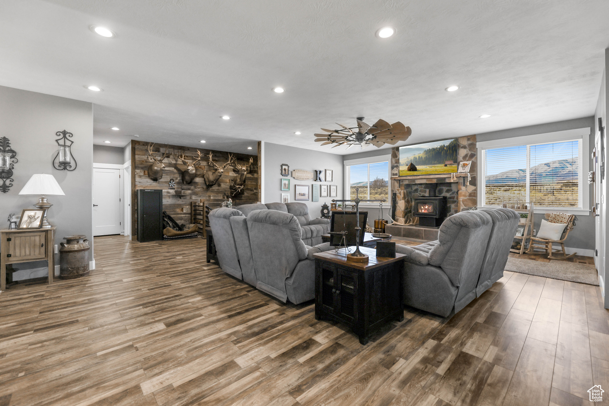 Living room with wood-type flooring, a stone fireplace, and ceiling fan