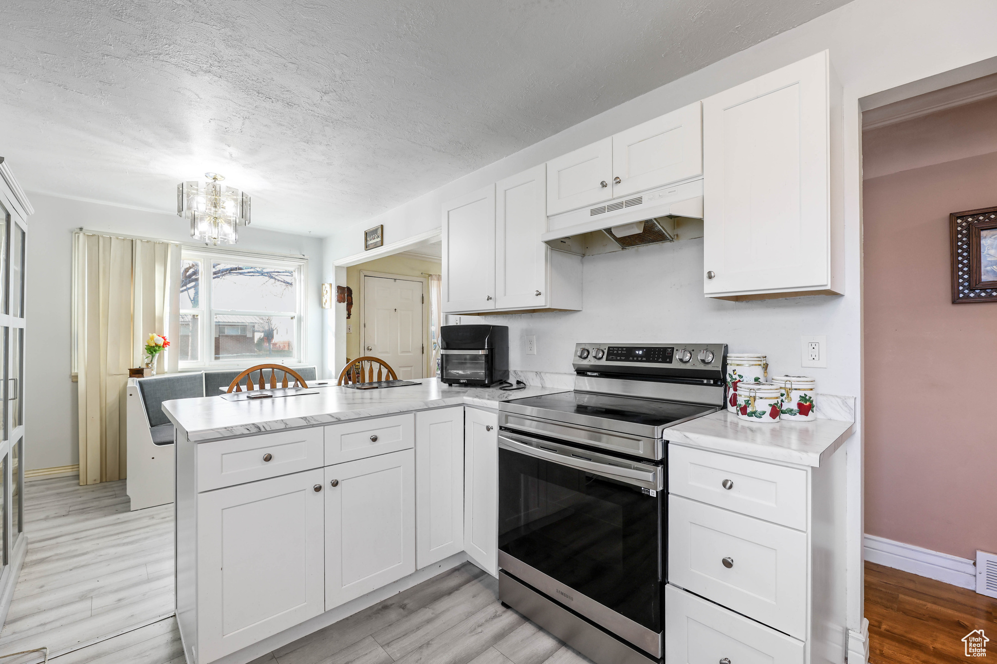 Kitchen featuring kitchen peninsula, light wood-type flooring, electric stove, white cabinets, and a chandelier