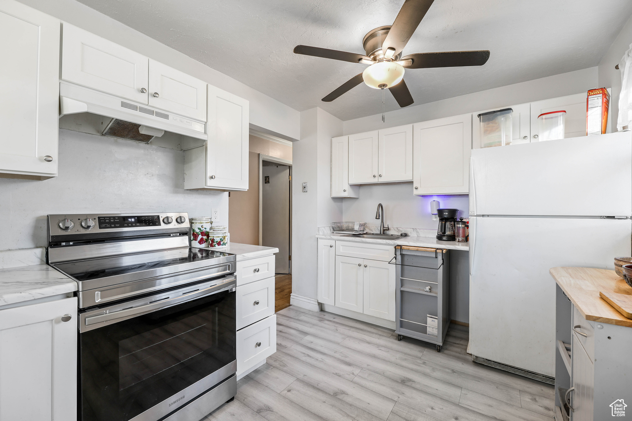 Kitchen featuring stainless steel electric range oven, sink, white refrigerator, white cabinets, and light wood-type flooring