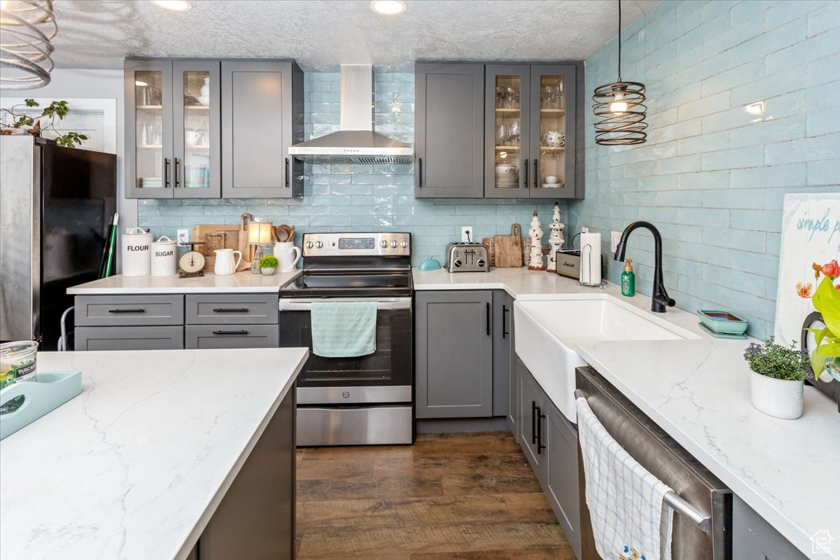 ADU Kitchen with gray cabinetry, sink, stainless steel appliances, hanging light fixtures, and wall chimney range hood