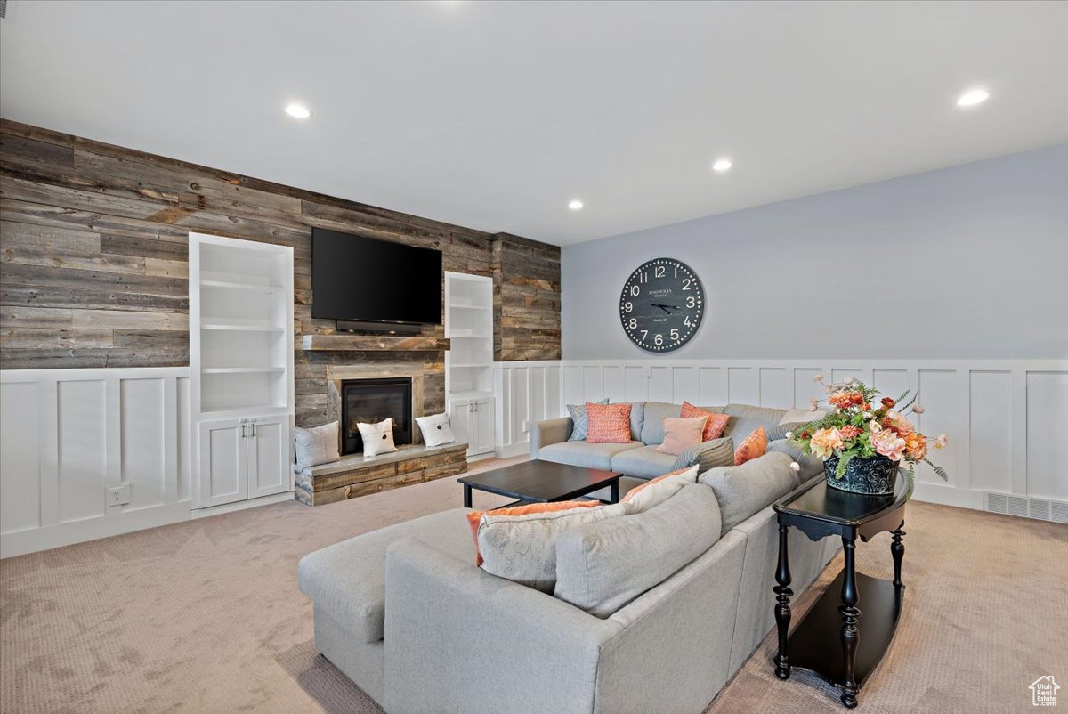 Carpeted living room with a fireplace, built in shelves, and wooden walls