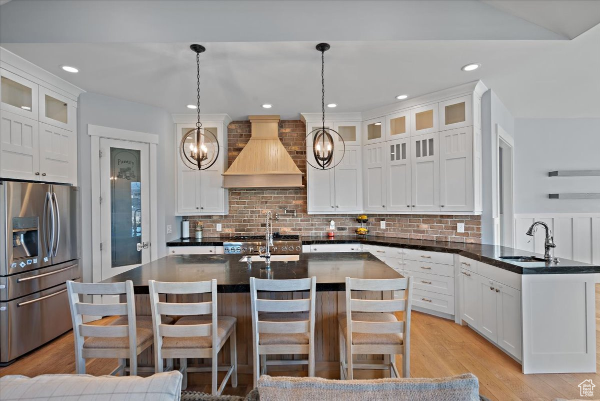 Kitchen with pendant lighting, a breakfast bar, premium range hood, sink, and stainless steel refrigerator with ice dispenser