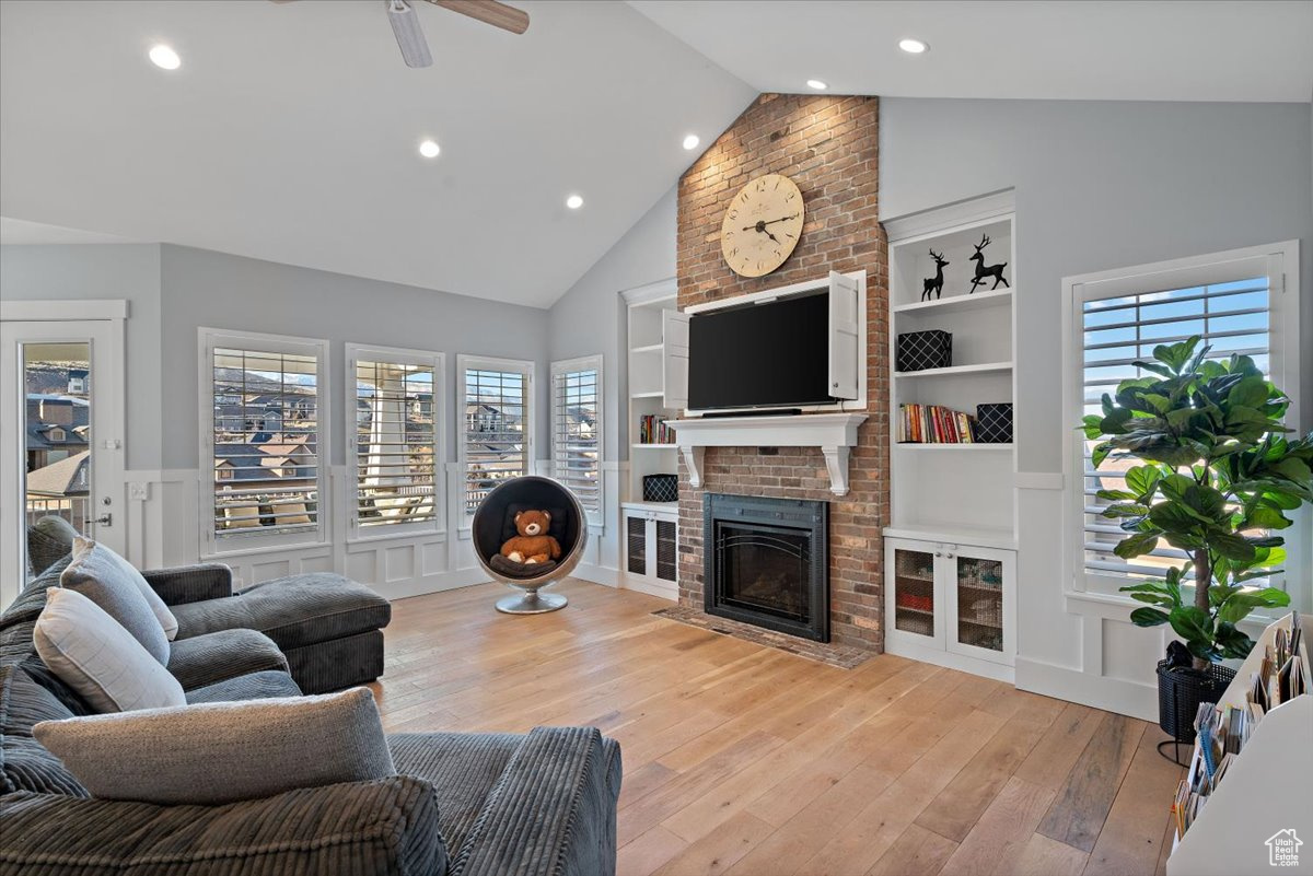 Living room with light wood-type flooring, built in shelves, ceiling fan, a fireplace, and lofted ceiling