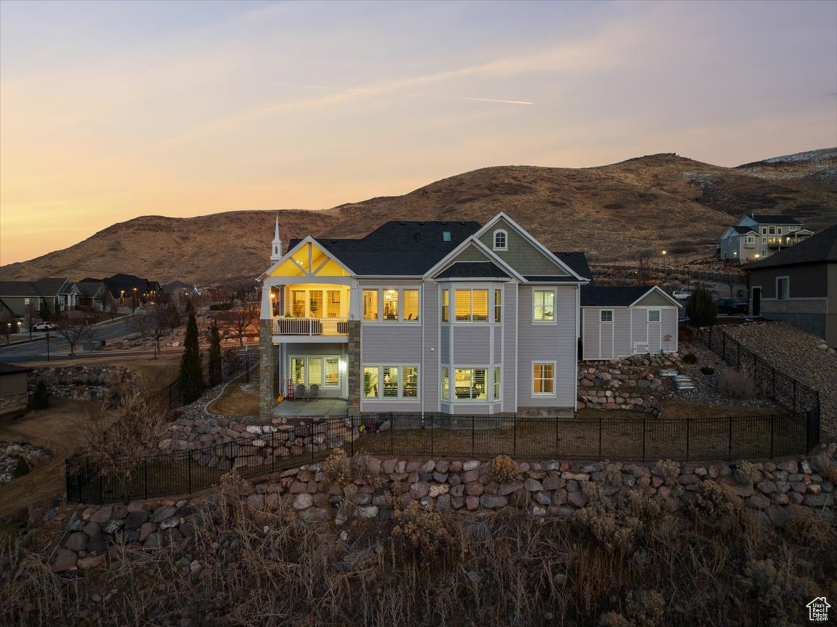 Back house at dusk featuring a mountain view, a patio, and a balcony