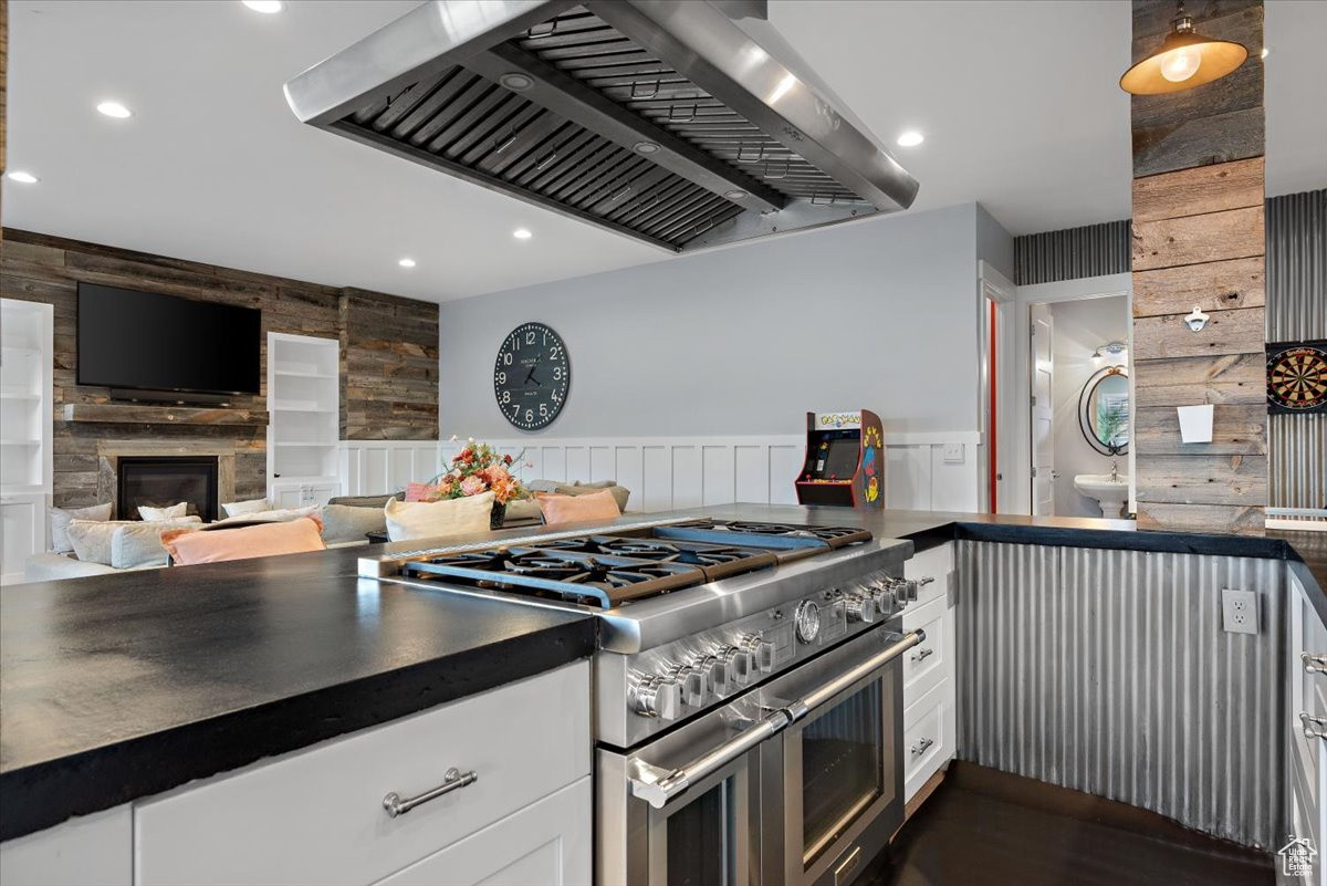 Kitchen with wood walls, double oven range, white cabinets, wall chimney exhaust hood, and a large fireplace