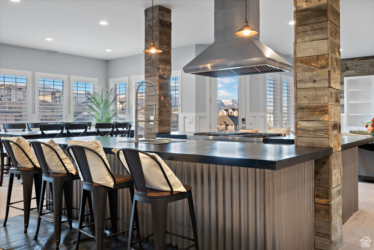 Kitchen featuring island exhaust hood, decorative columns, a breakfast bar area, and sink