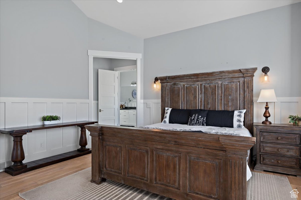 Bedroom featuring ensuite bathroom, light wood-type flooring, and vaulted ceiling