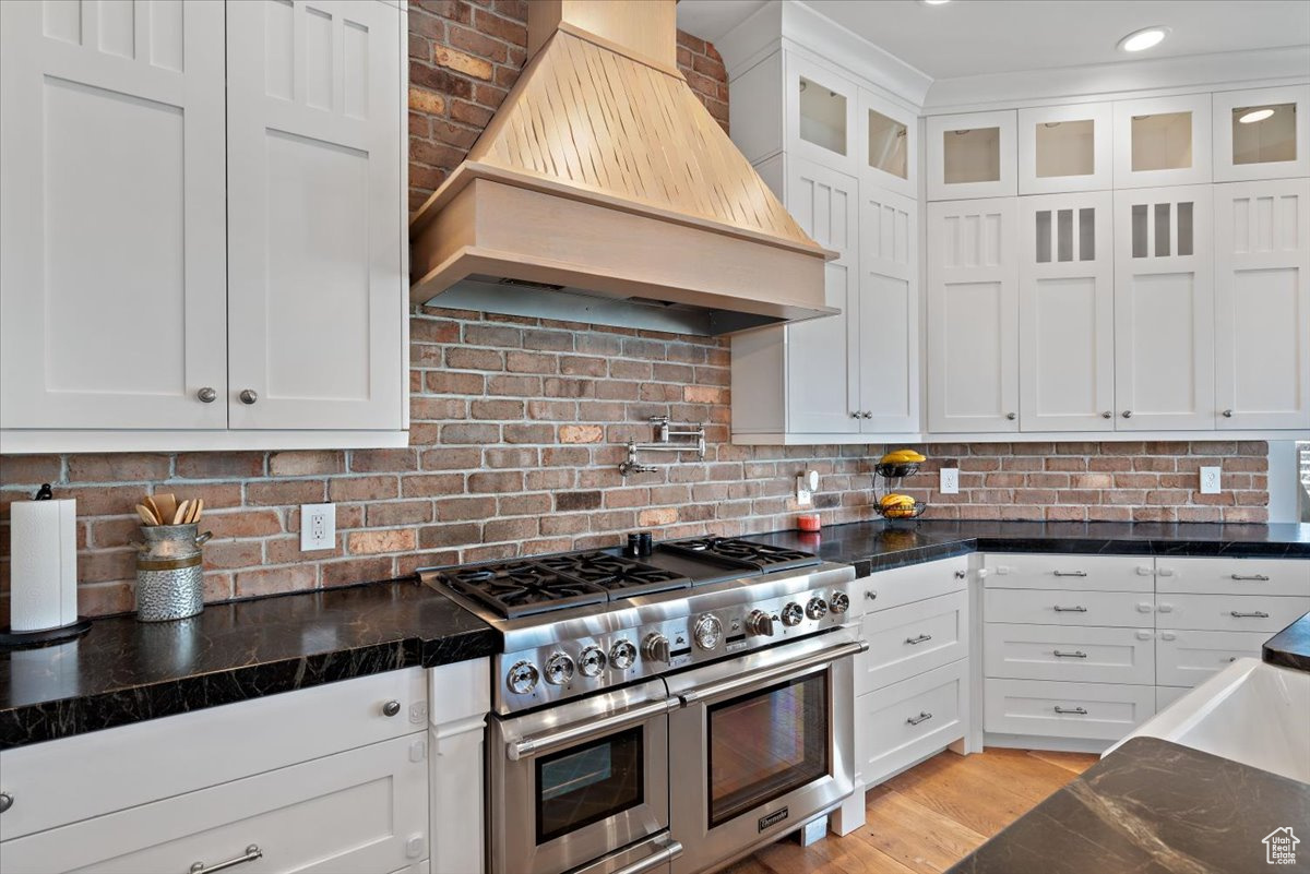 Kitchen featuring custom exhaust hood, double oven range, and white cabinetry