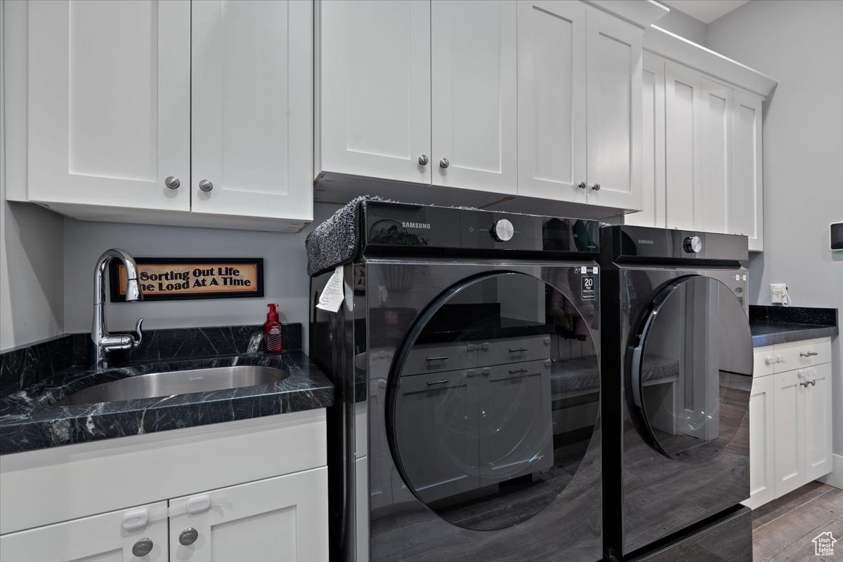 Clothes washing area with dark hardwood / wood-style flooring, washer and dryer, sink, and cabinets