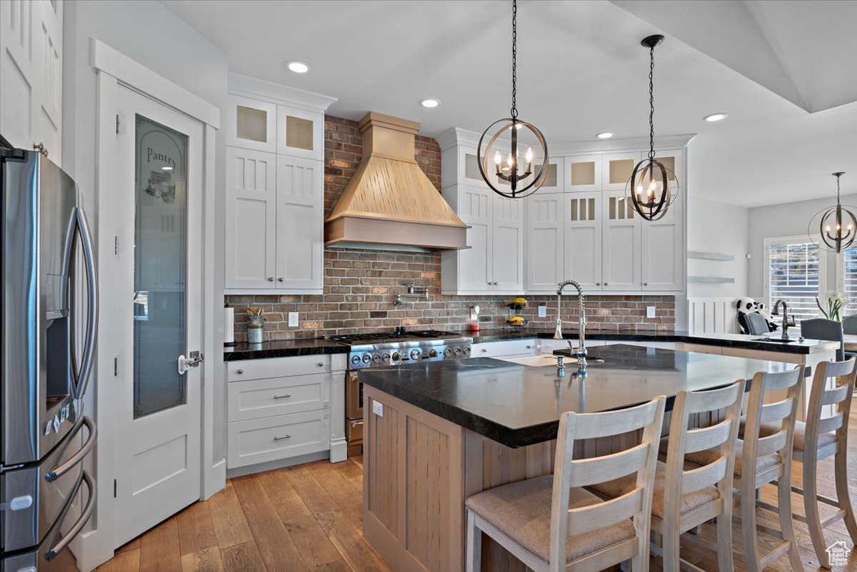 Kitchen with a kitchen island with sink, white cabinetry, stainless steel appliances, and custom range hood