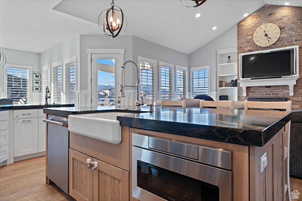 Kitchen featuring a kitchen island, stainless steel dishwasher, a notable chandelier, decorative light fixtures, and white cabinets