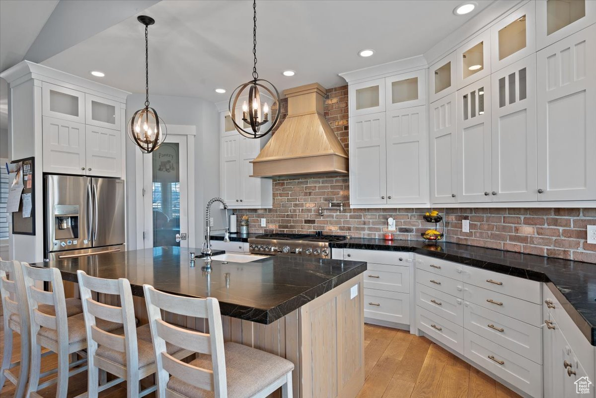 Kitchen with a kitchen island with sink, a kitchen bar, decorative backsplash, custom exhaust hood, and appliances with stainless steel finishes