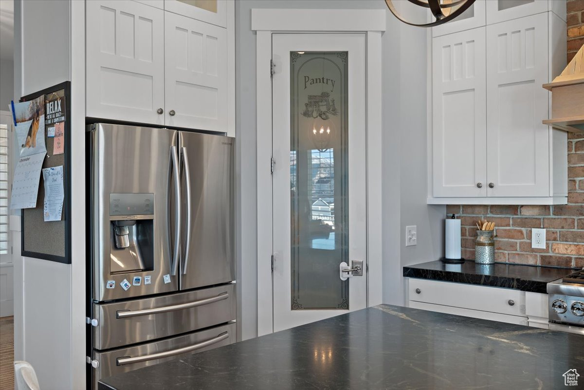 Kitchen featuring stainless steel refrigerator with ice dispenser, tasteful backsplash, and white cabinetry