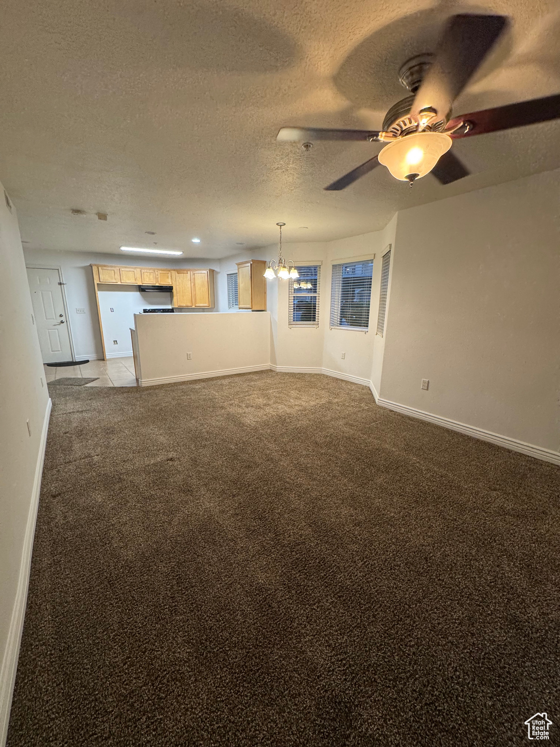 Unfurnished living room with ceiling fan with notable chandelier, light colored carpet, and a textured ceiling