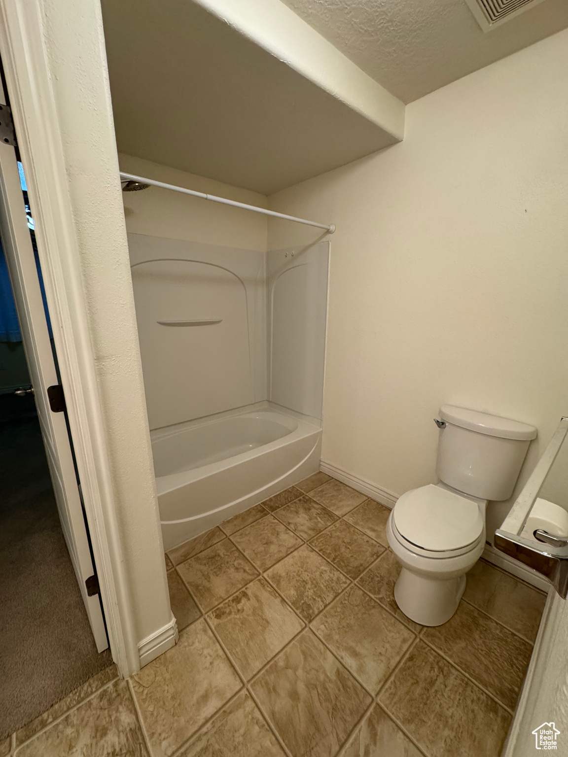 Bathroom featuring washtub / shower combination, a textured ceiling, and toilet