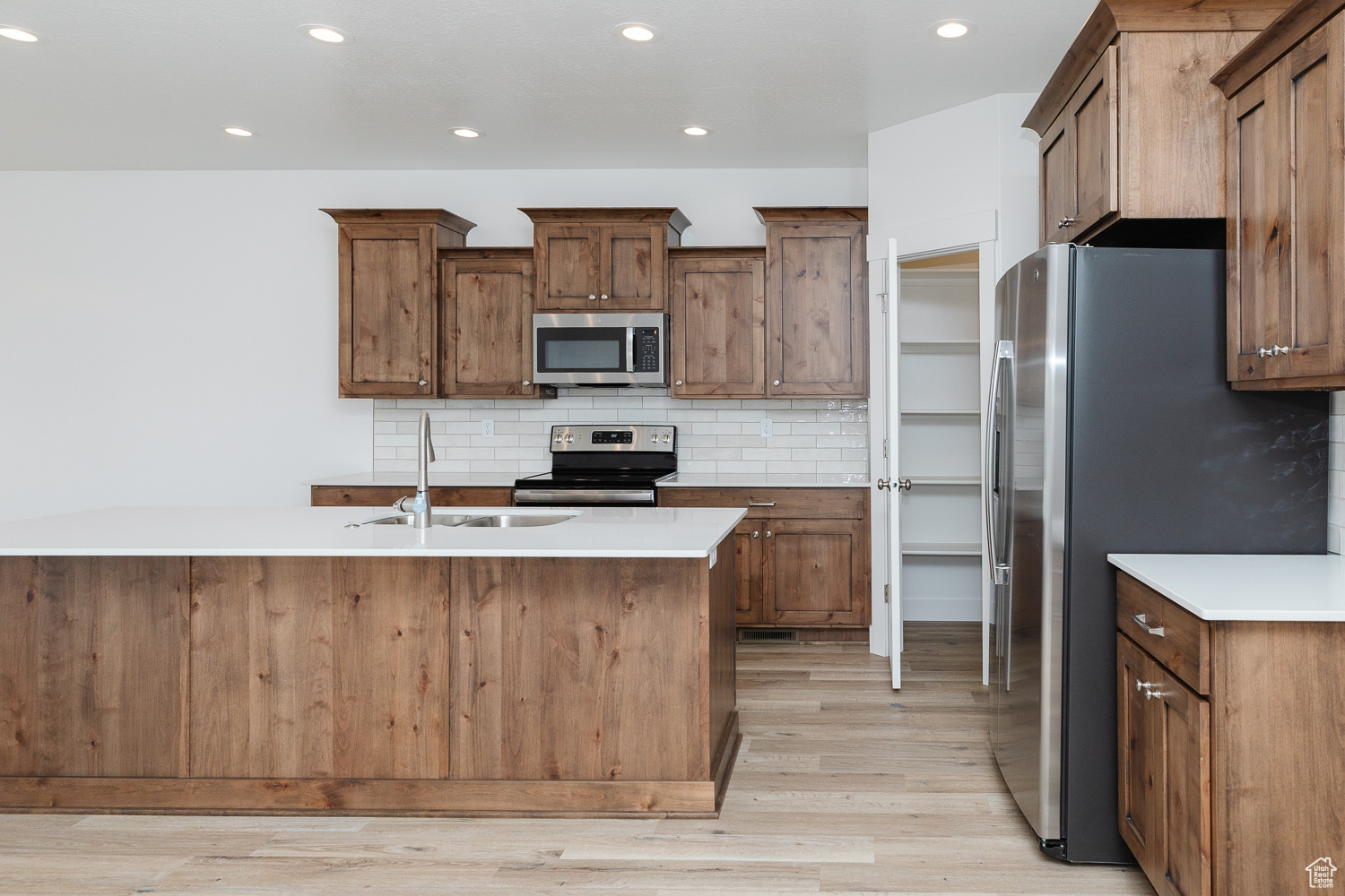 Kitchen with sink, stainless steel appliances, light hardwood / wood-style flooring, an island with sink, and decorative backsplash