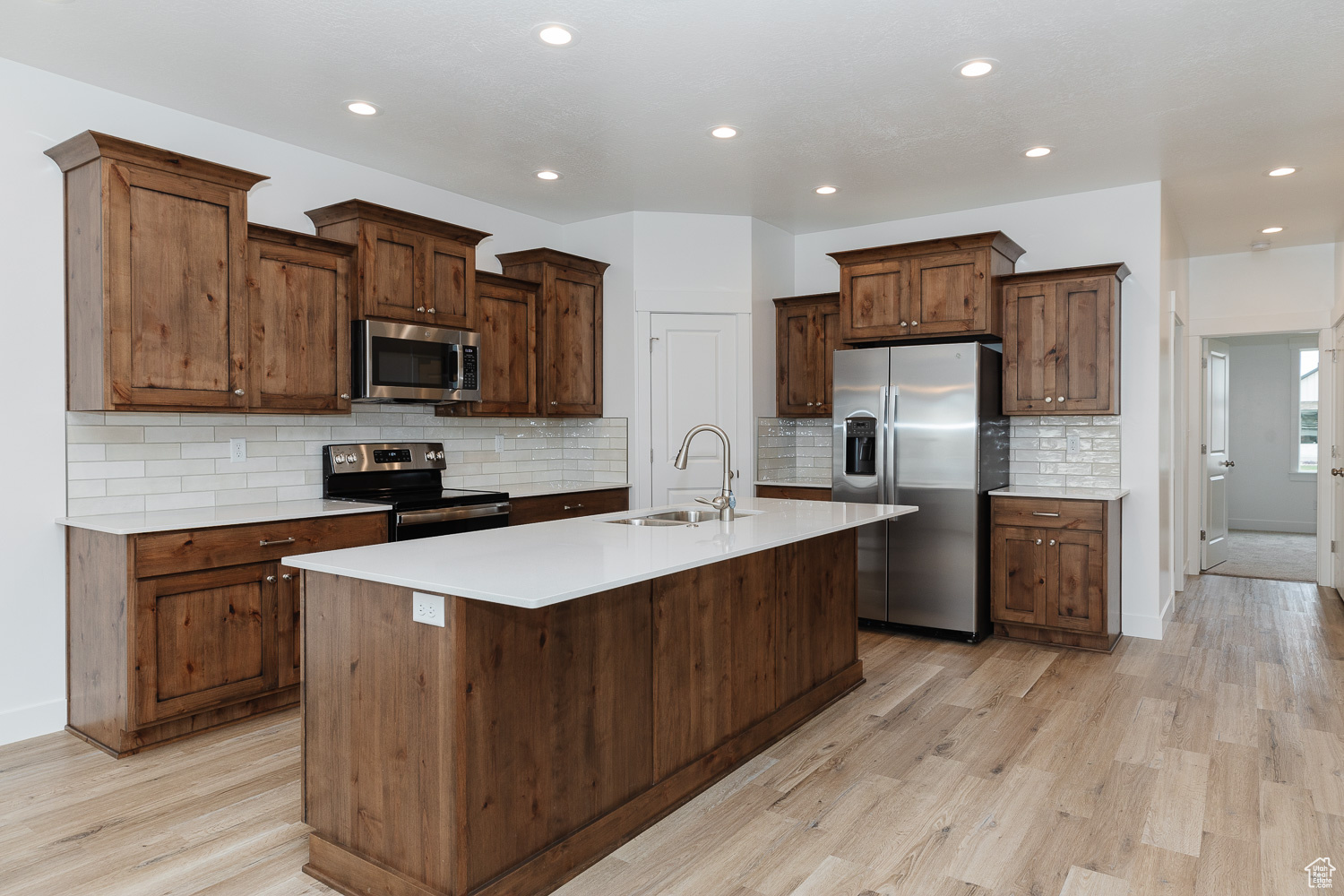 Kitchen with backsplash, a center island with sink, sink, light hardwood / wood-style flooring, and appliances with stainless steel finishes
