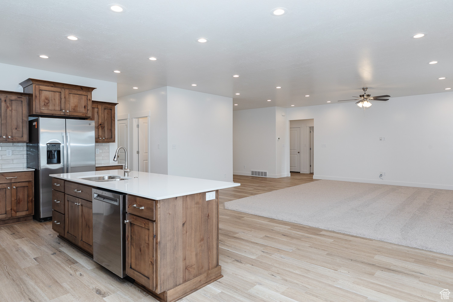 Kitchen featuring decorative backsplash, appliances with stainless steel finishes, ceiling fan, a kitchen island with sink, and sink