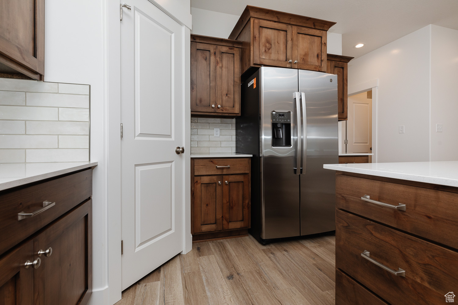 Kitchen with stainless steel fridge with ice dispenser, light wood-type flooring, and tasteful backsplash