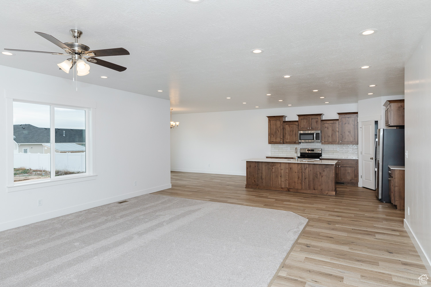 Kitchen featuring ceiling fan, an island with sink, decorative backsplash, appliances with stainless steel finishes, and light wood-type flooring