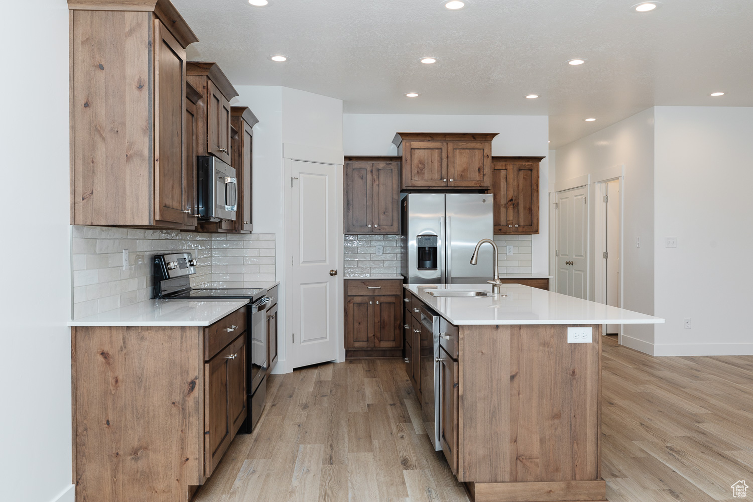Kitchen with decorative backsplash, appliances with stainless steel finishes, a kitchen island with sink, sink, and light hardwood / wood-style flooring