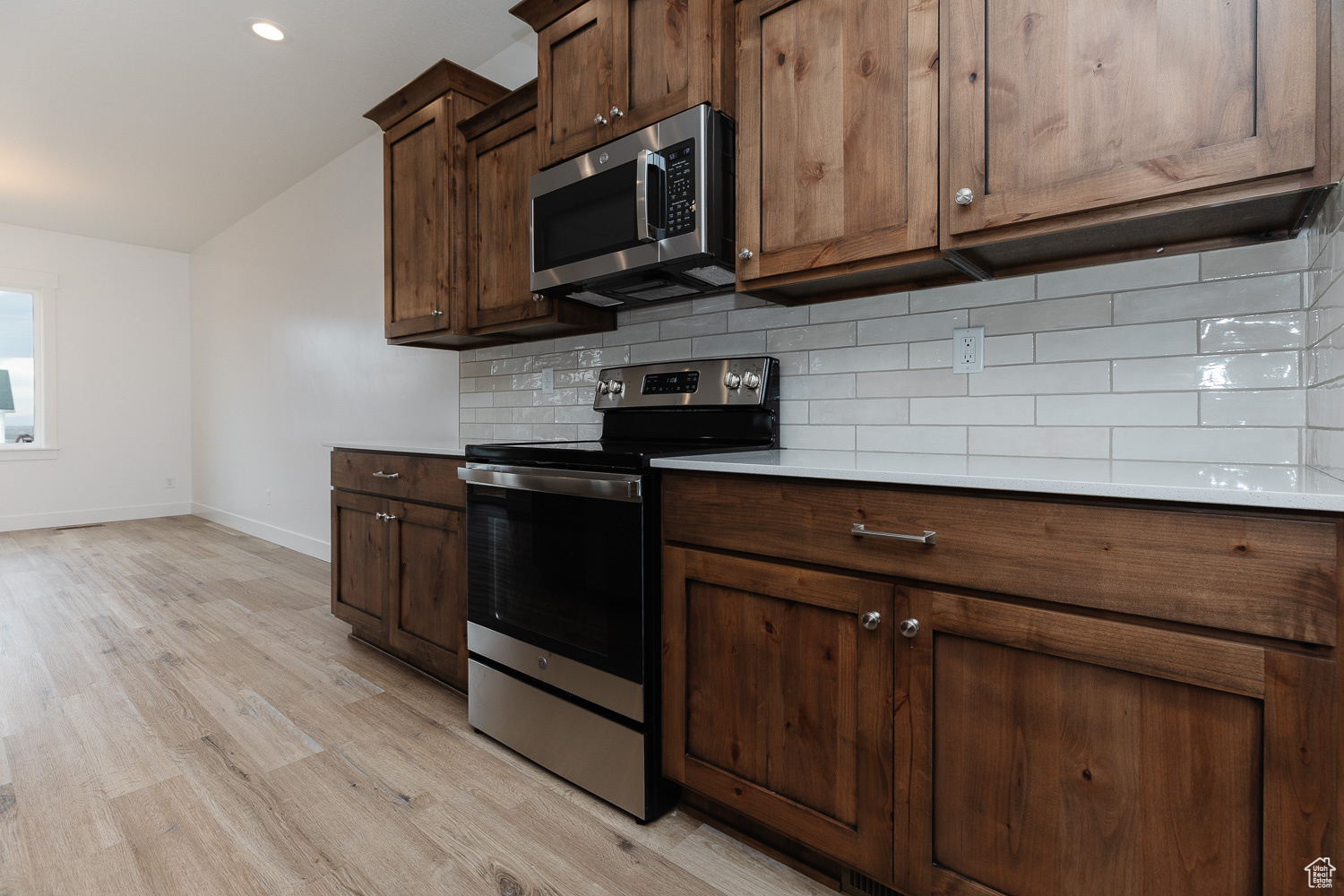 Kitchen with backsplash, dark brown cabinets, stainless steel appliances, and light hardwood / wood-style floors