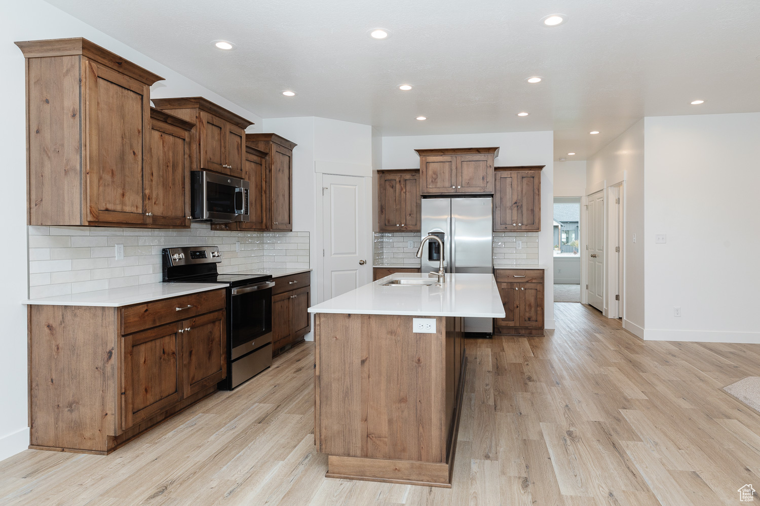 Kitchen with a kitchen island with sink, sink, light hardwood / wood-style floors, and appliances with stainless steel finishes
