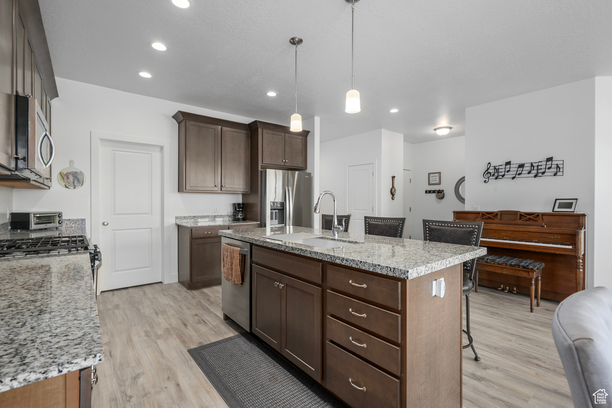 Kitchen featuring light stone countertops, appliances with stainless steel finishes, a kitchen island with sink, sink, and pendant lighting